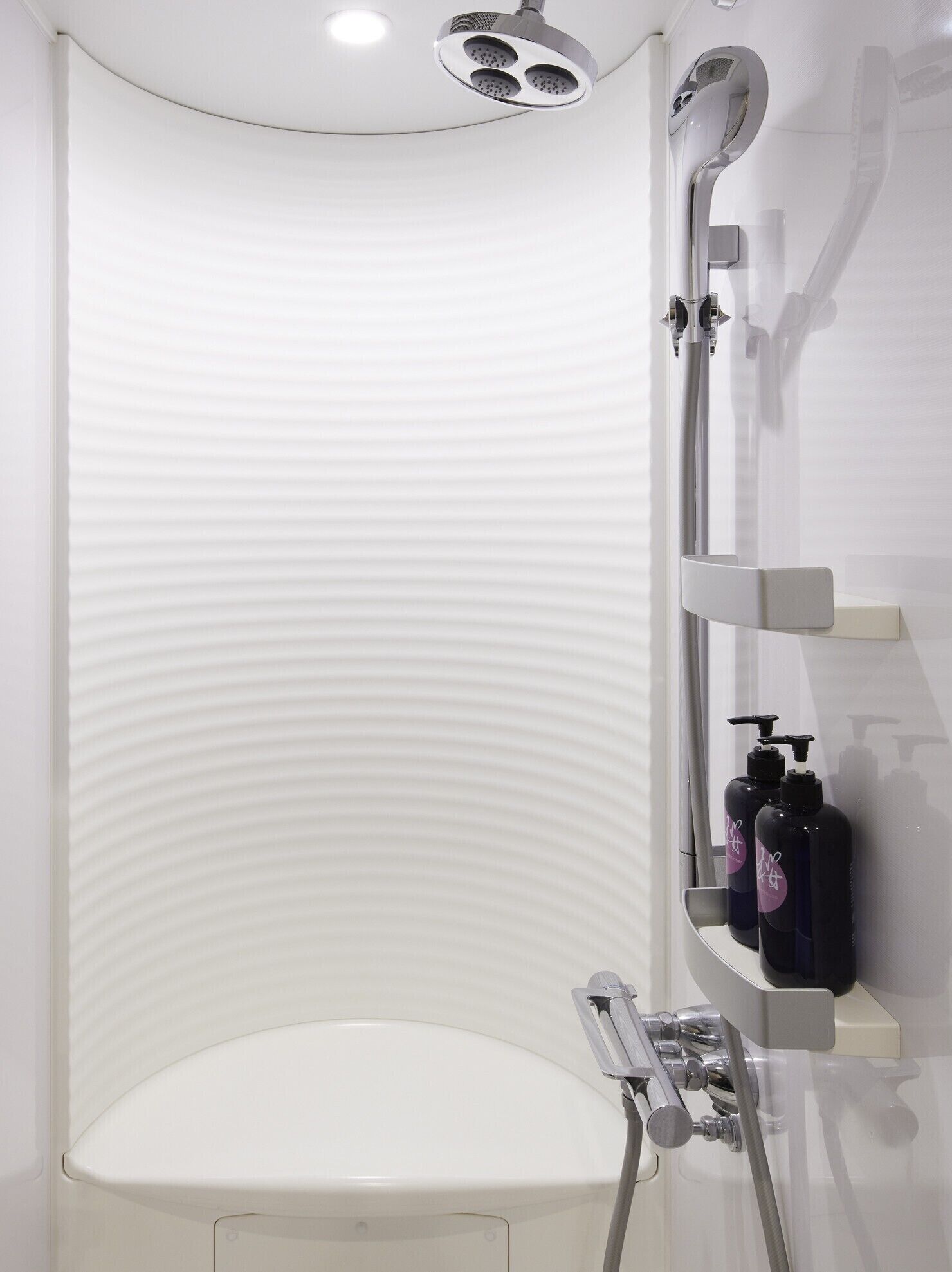 Un bagno moderno con cabina doccia a forma di arco, un water e un dispenser di sapone fissato alla parete.