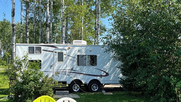 A recreational vehicle (RV) parked in a grassy area with a small table and two chairs. - Eagle- Camper at Sunset Bay  (Onanole)