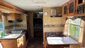 A compact RV kitchen with wooden cabinets, a sink, stove, and a small dining area. - Eagle- Camper at Sunset Bay  (Onanole)
