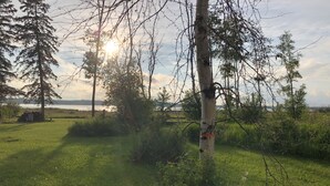 A grassy outdoor area with trees and a view of a body of water. - Eagle- Camper at Sunset Bay  (Onanole)