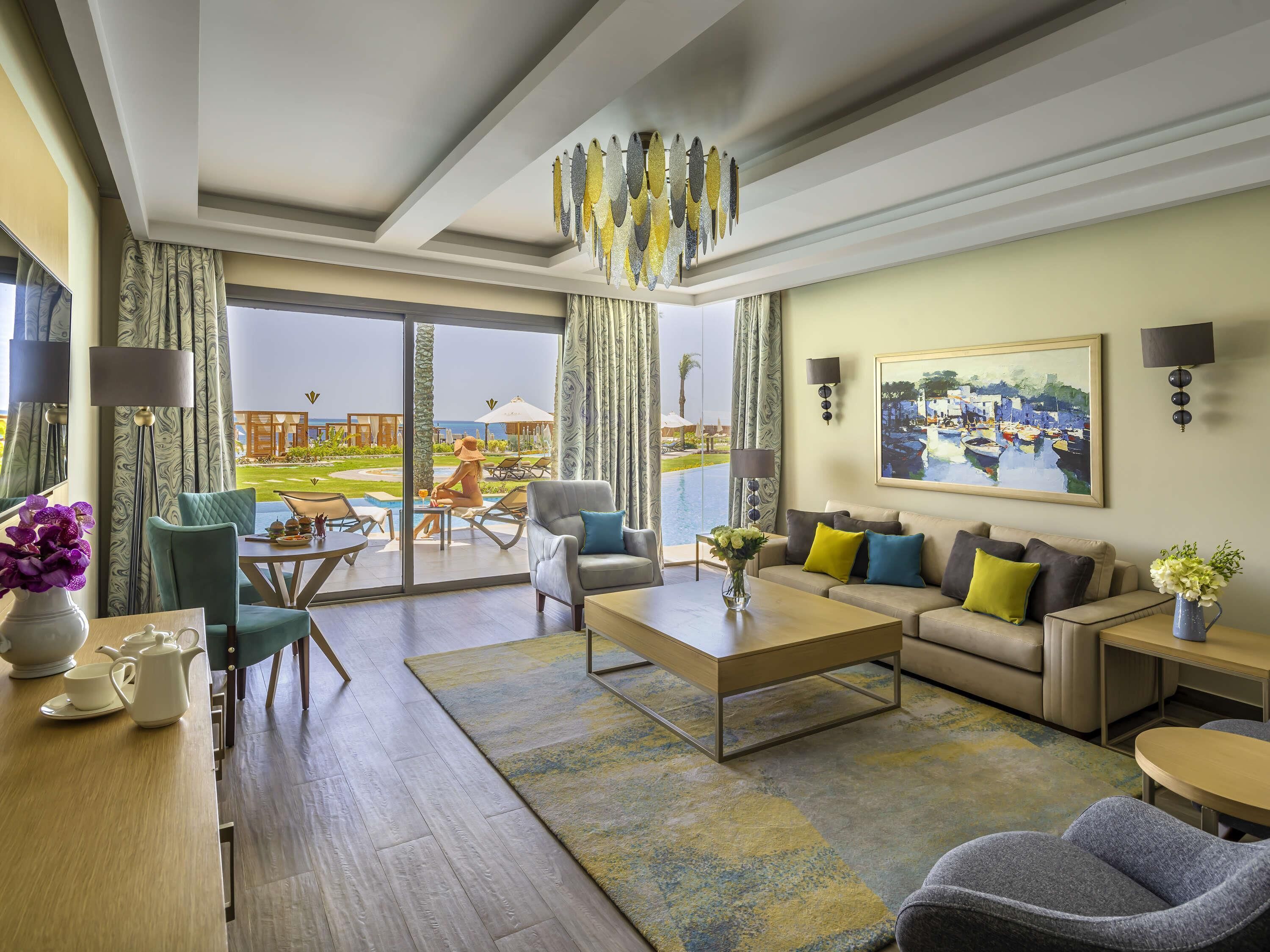 A spacious living room with a large window, a sofa, a coffee table, and a view of a pool and outdoor area.