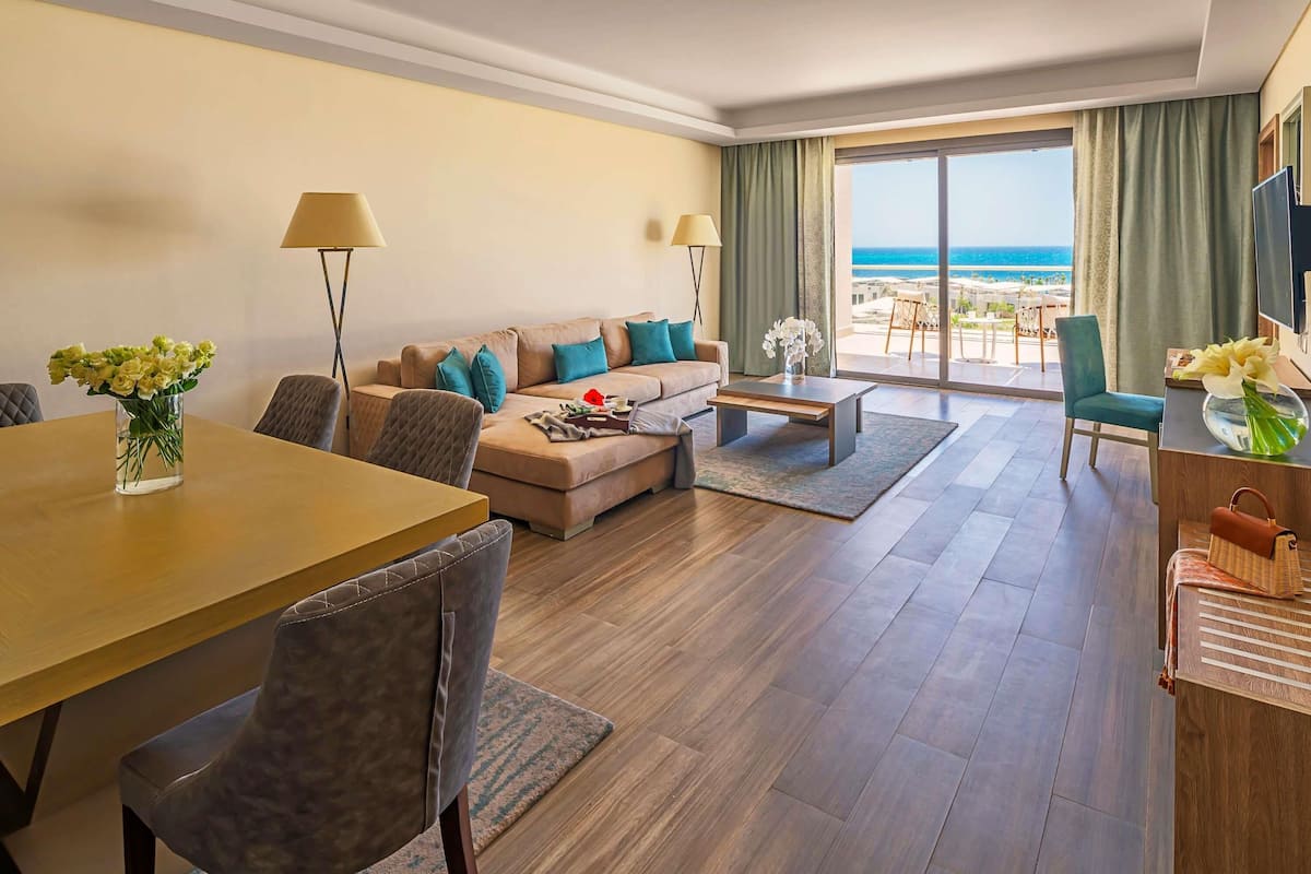 Ein Hotelzimmer mit Sofa, Esstisch, Stühlen, Couchtisch, Fernseher und Meerblick.