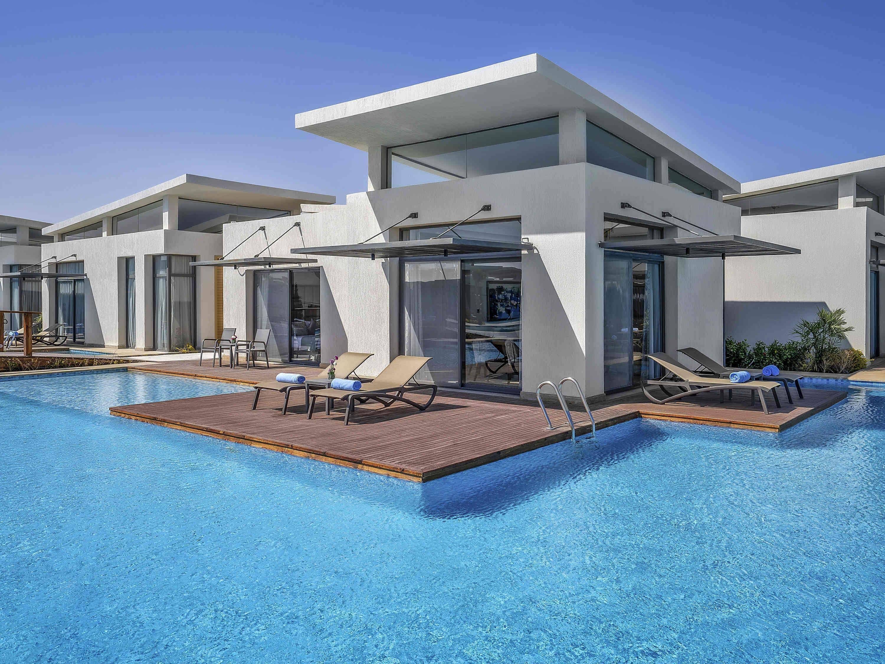Un hôtel moderne doté d’une piscine, de chaises longues et d’un espace salon couvert.