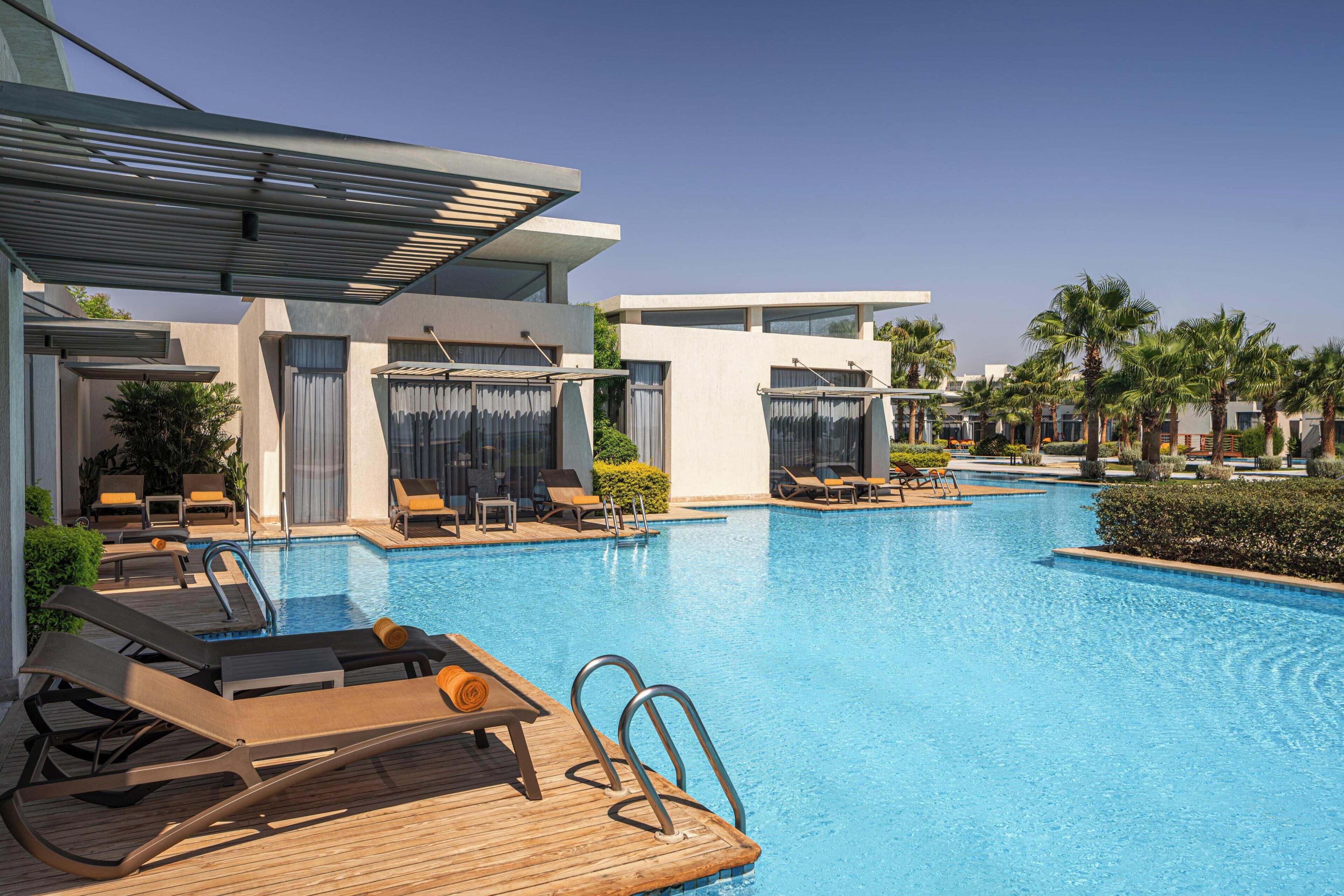 A modern hotel pool area with sun loungers, a wooden deck, and a clear blue pool.
