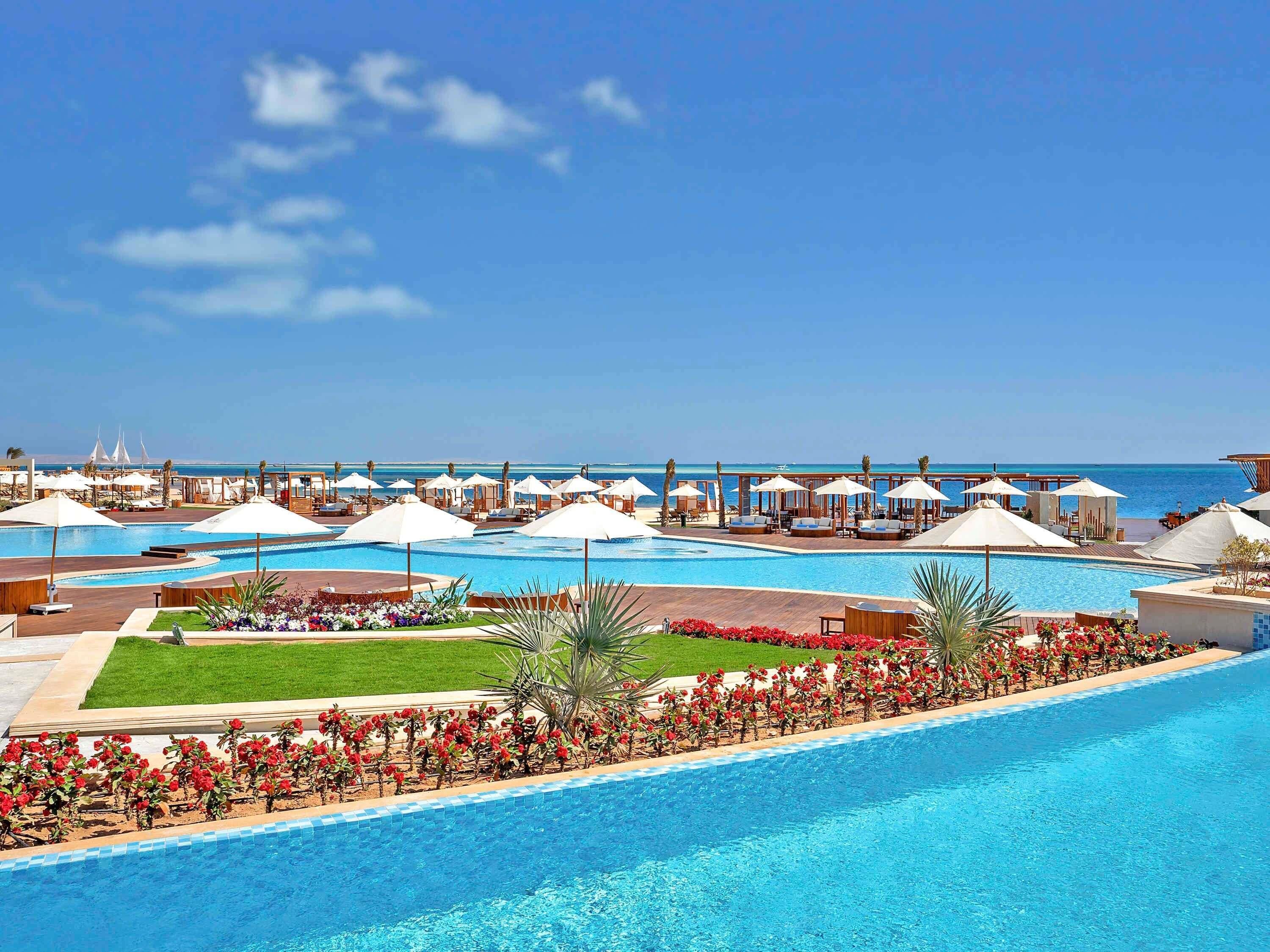 A resort with multiple swimming pools, lounge areas, and a view of the sea.