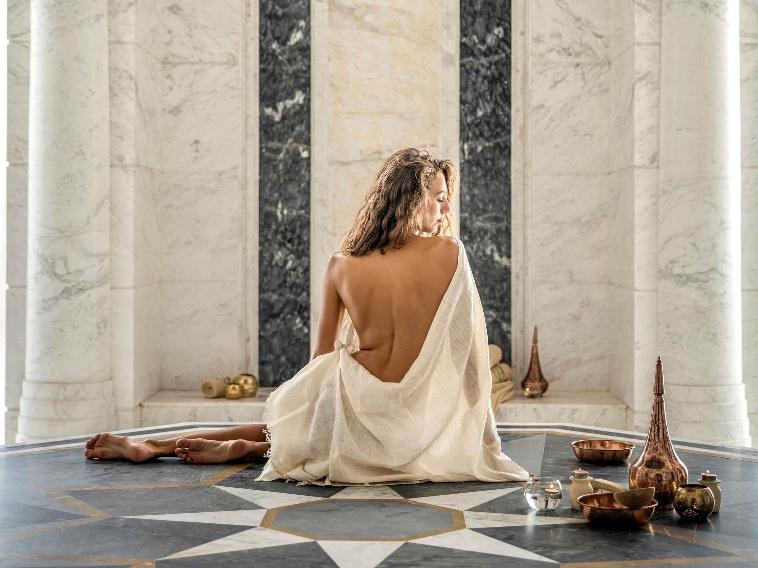A person sitting on a patterned floor with columns, surrounded by various objects.