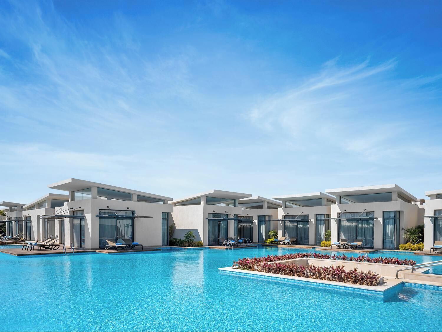 Un hôtel moderne doté d’une piscine, de chaises longues et offrant une vue sur un ciel bleu azur.