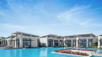 Un hôtel moderne doté d’une piscine, de chaises longues et offrant une vue sur un ciel bleu azur.
