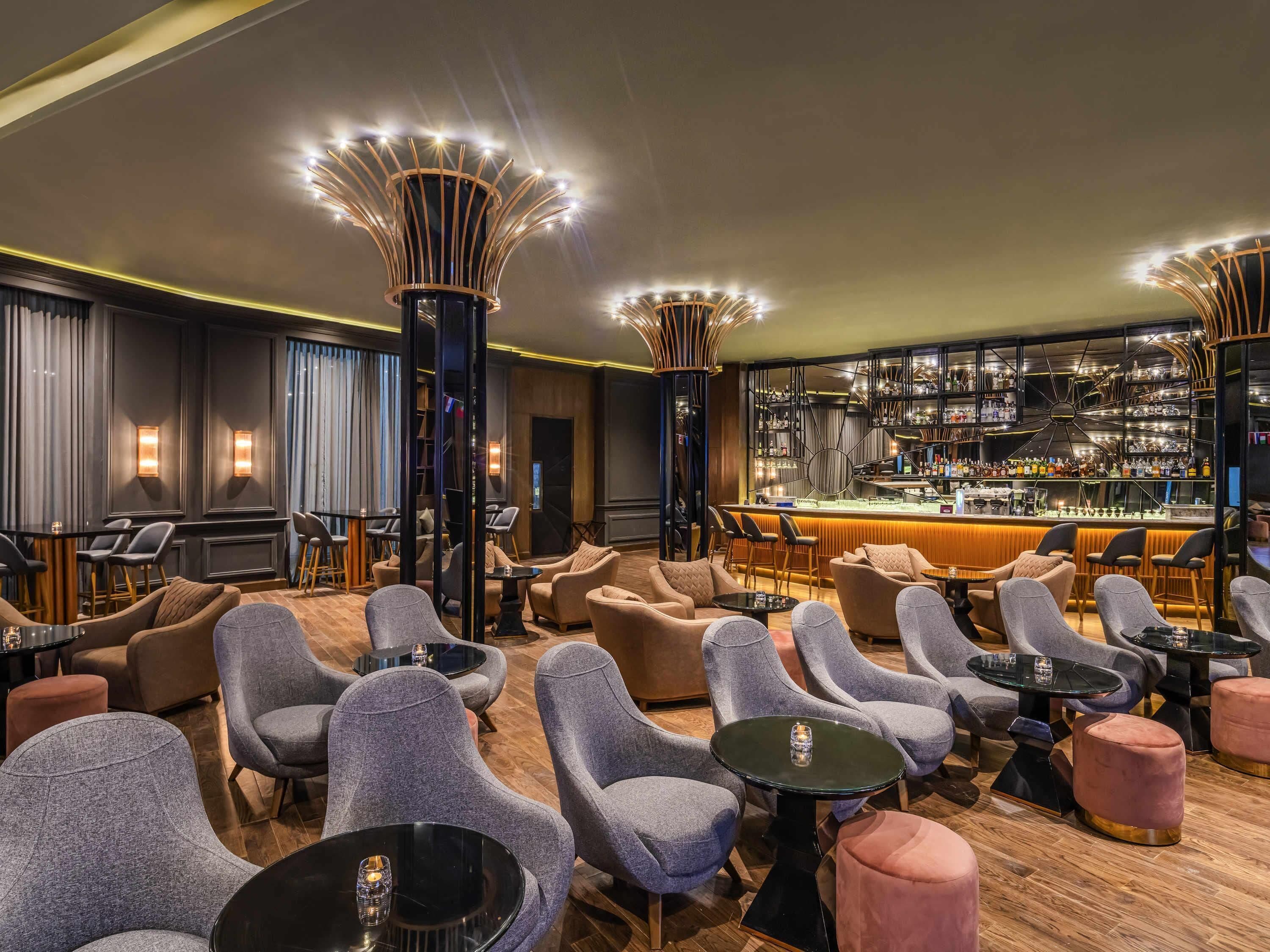 A modern bar area with a variety of seating options, including sofas and chairs, and a well-stocked bar with numerous bottles and glasses.