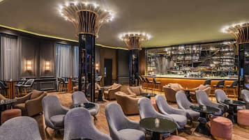 A modern bar area with a variety of seating options, including sofas and chairs, and a well-stocked bar with numerous bottles and glasses.