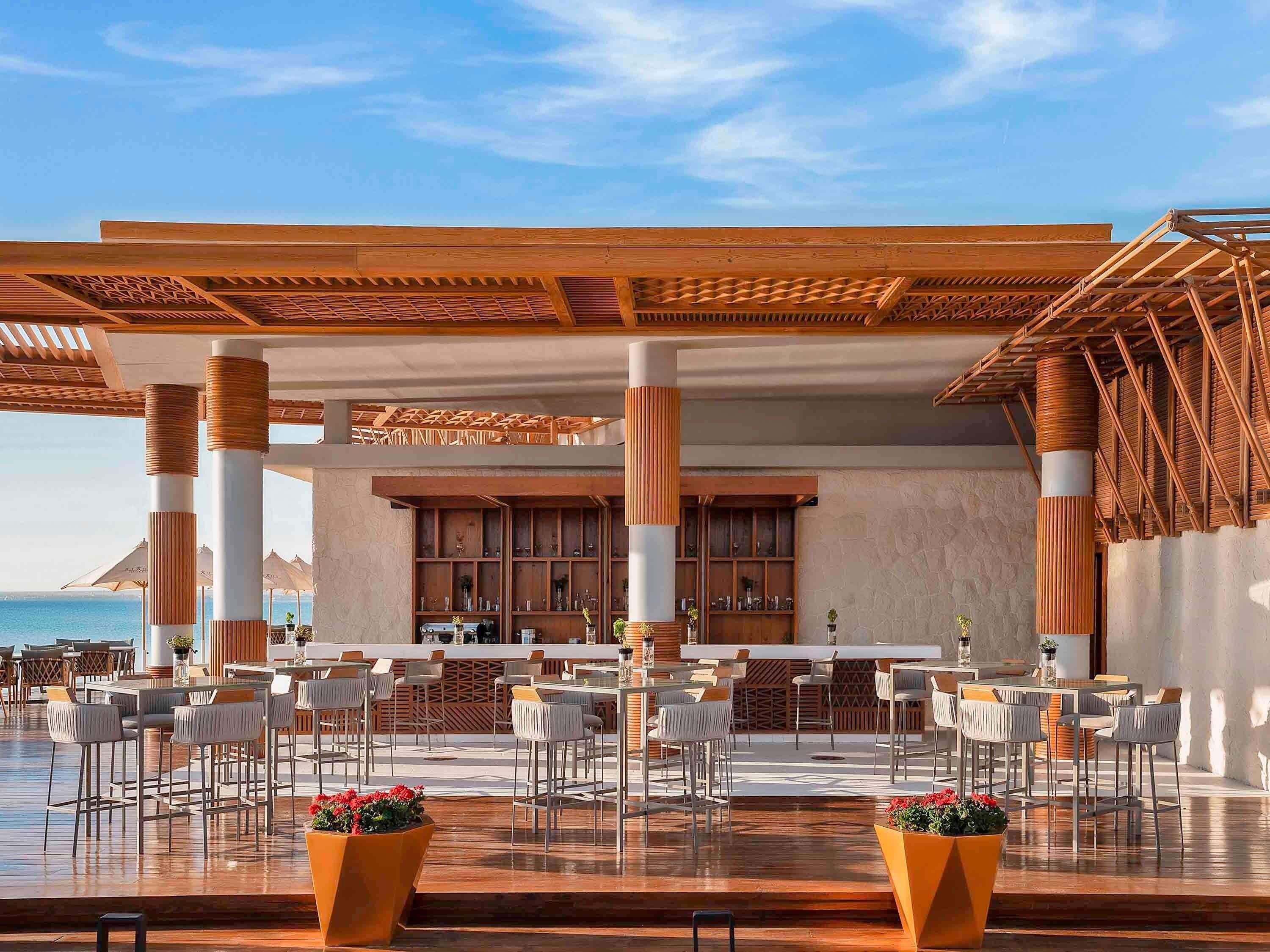 Un espace extérieur abrité, aménagé avec des tables et des chaises, un bar et offrant une vue sur la mer.