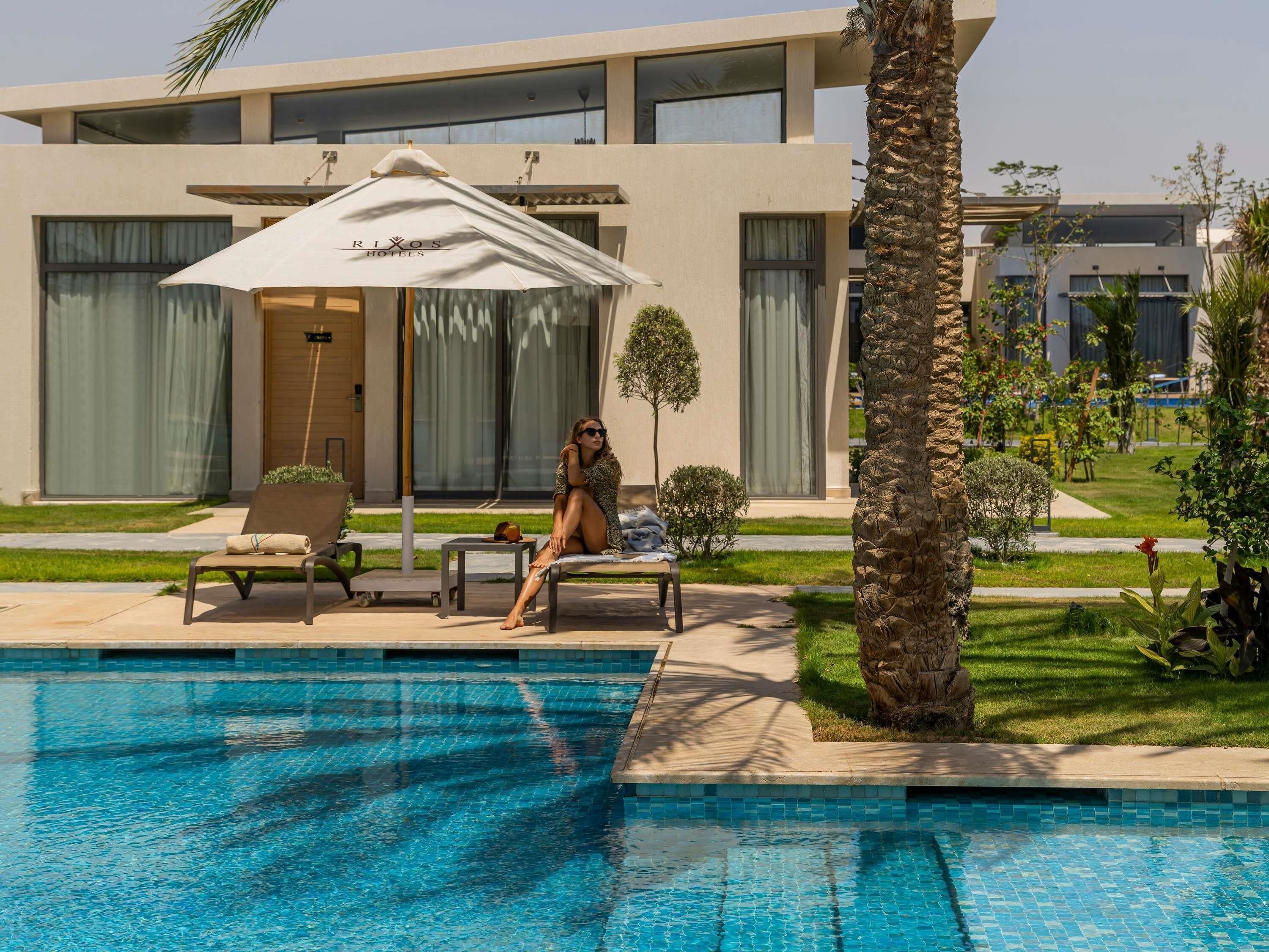 A modern hotel with a pool, outdoor seating, and a palm tree.