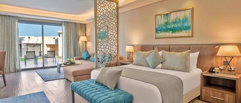 Habitación de hotel con una cama grande, zona de estar con un banco y vistas al exterior.