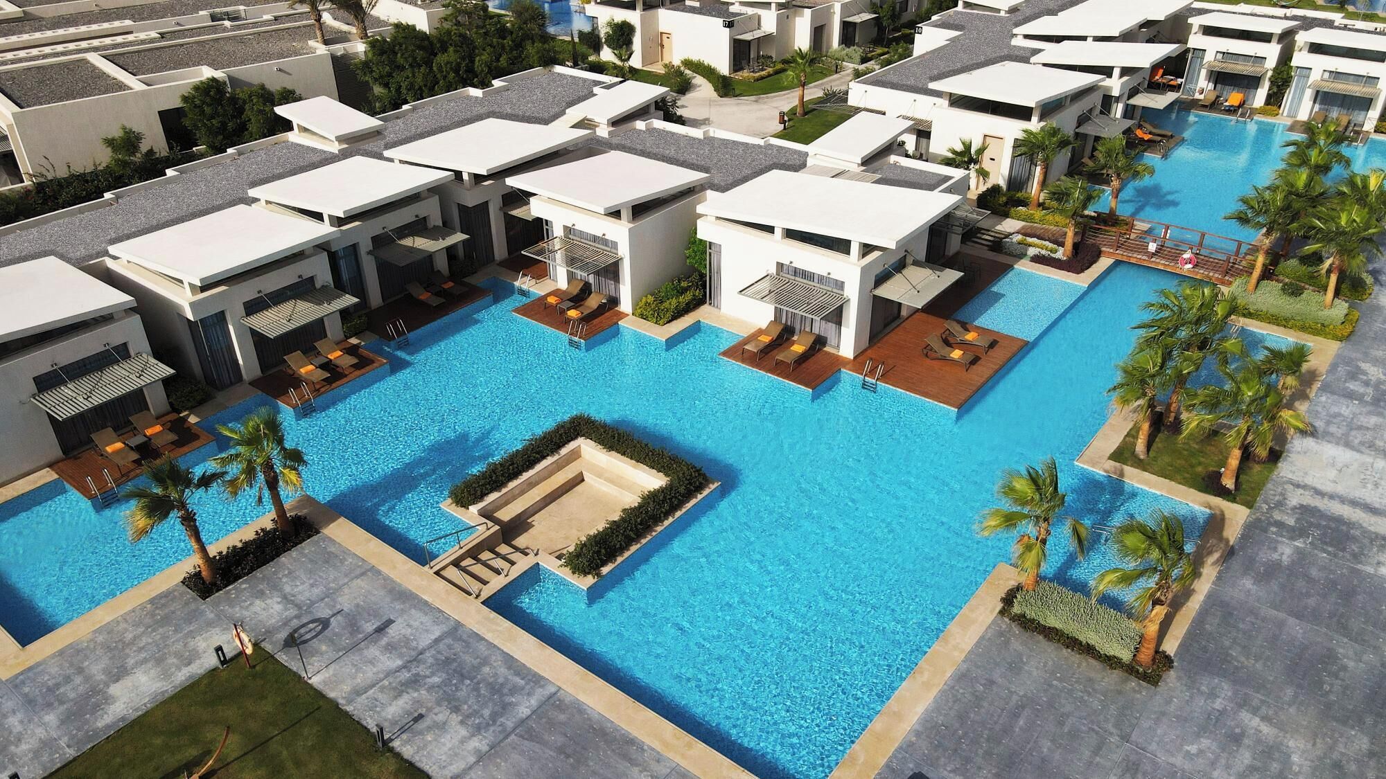 A modern hotel with a central swimming pool, multiple balconies, and a landscaped pool area.