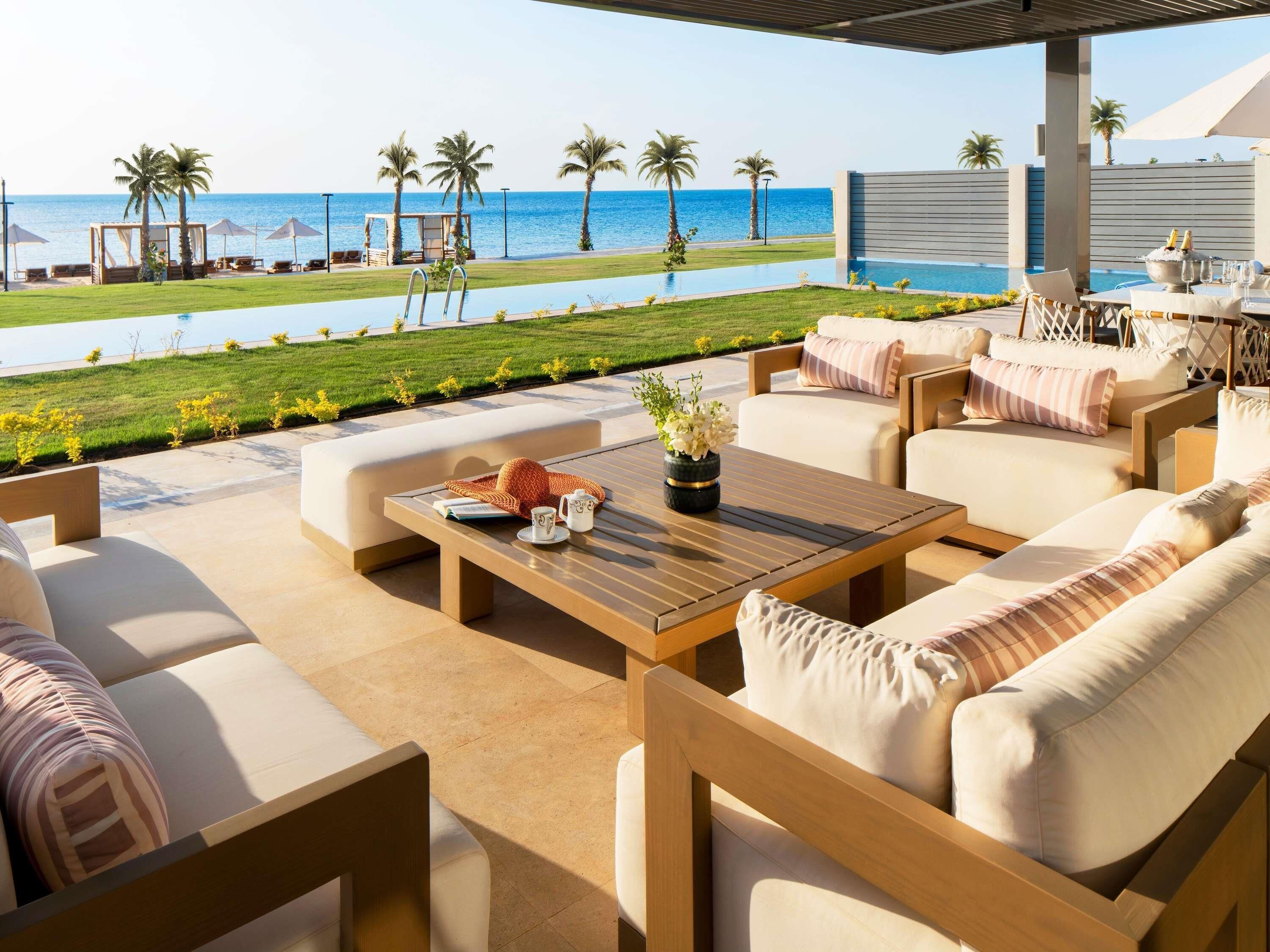 A poolside area with outdoor seating, a view of the sea, and a covered dining area.