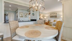 Een eetgedeelte met een ronde tafel, rieten stoelen en een kroonluchter.