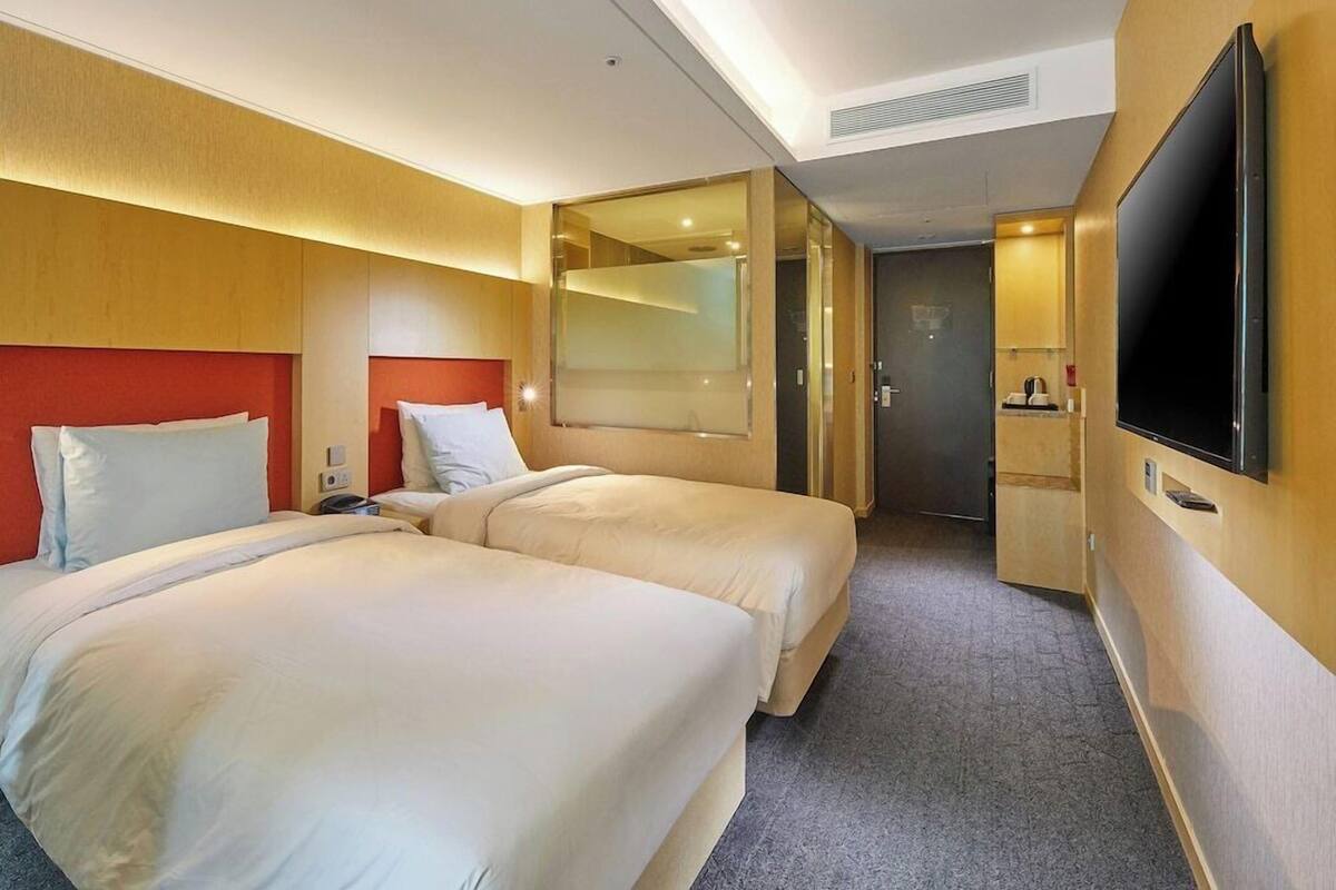 A hotel room with two beds, a TV, a mirror, and a door leading to a bathroom.