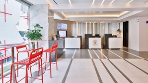 Una zona d'entrada moderna, amb taulell de recepció, pantalla digital i espai d'espera amb cadires vermelles.