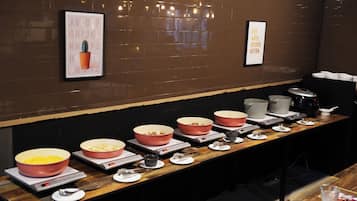A buffet setup with multiple bowls of food, weighing scales, and a variety of utensils on a wooden table.