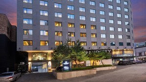 Un edifici d'hotel modern amb façana plana, diverses finestres i una zona d'aparcament al davant.