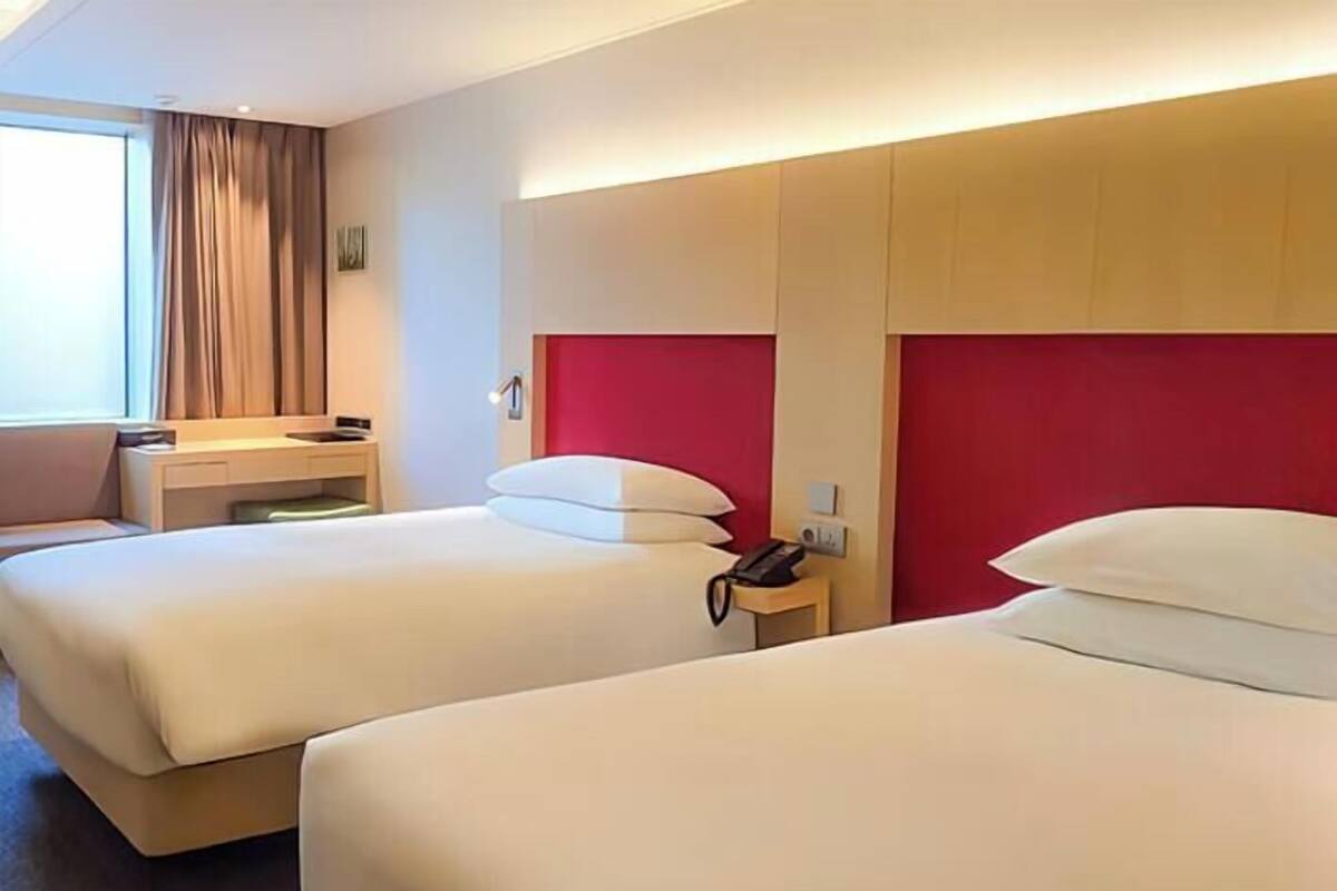 A hotel room with two beds, a desk, a telephone, and a window with curtains.