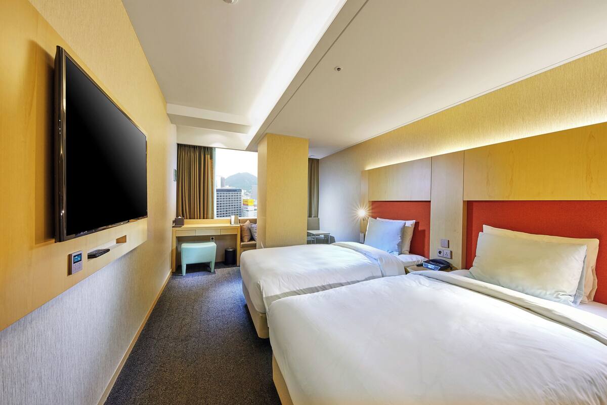 A hotel room with two beds, a desk, a TV, and a city view.