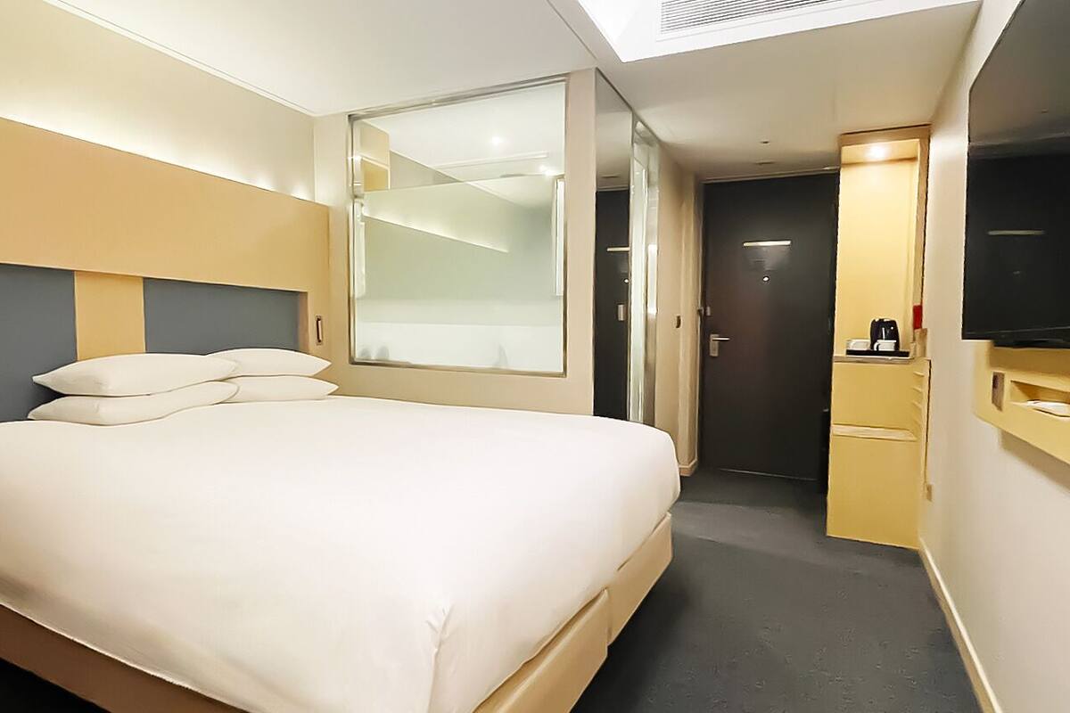 A hotel room with a bed, a TV, a desk, and a door.