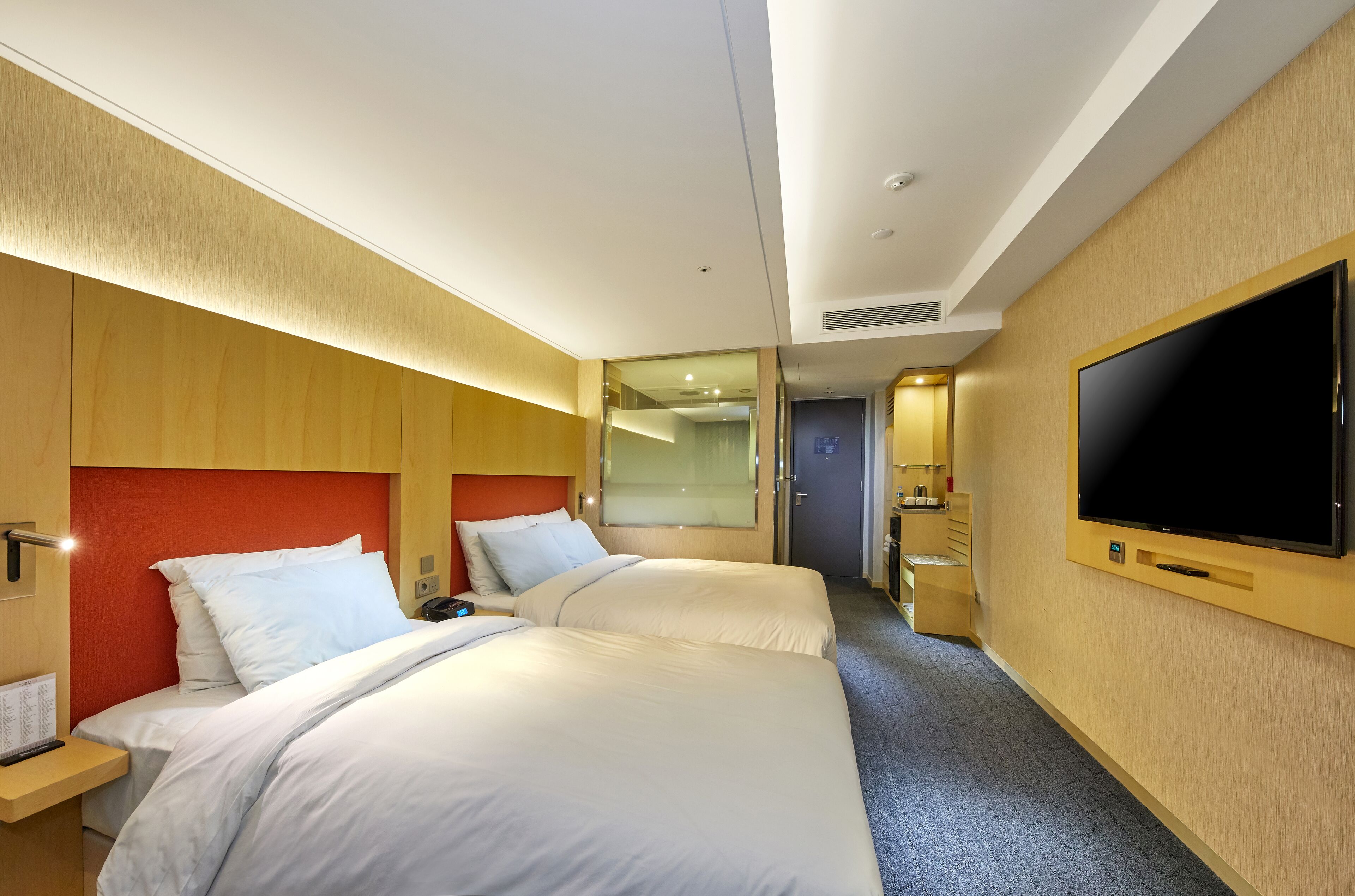 Quarto de hotel com duas camas, uma televisão grande e um espelho.