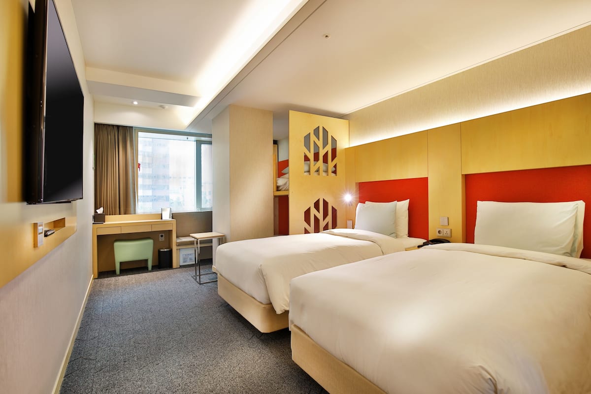 A hotel room with two beds, a desk, a chair, and a TV.