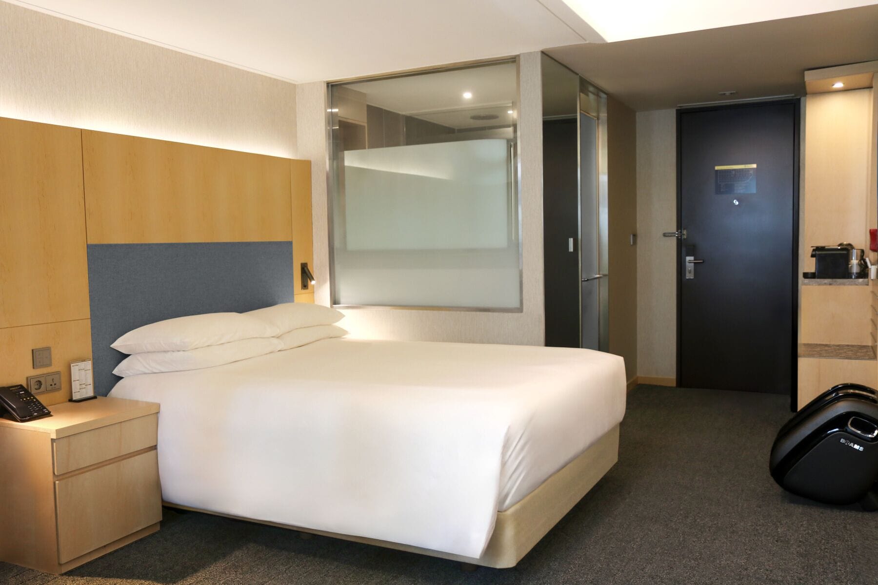 Una habitación de hotel con una cama, un escritorio con teléfono, un espejo y una puerta.