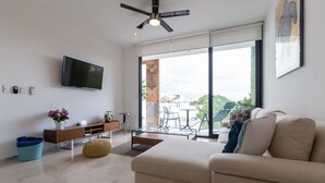 En moderne stue med et fladskærms-tv, en sofa, et sofabord og et spiseområde med bord og stole.