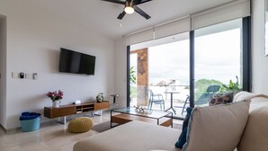 En moderne stue med sofa, sofabord i glas, fjernsyn ophængt på væggen og en balkon med udsigt.
