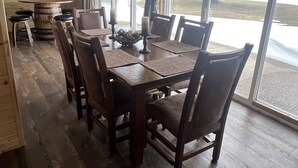 Un espace repas comprenant une table et des chaises en bois, un lustre et de grandes fenêtres donnant sur l’extérieur.