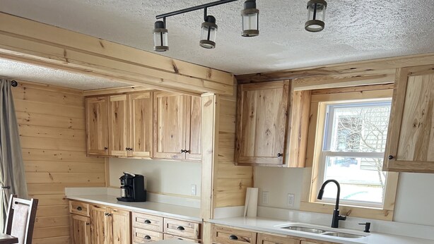 Une cuisine moderne avec des meubles en bois, un grand îlot central, des tabourets noirs et un lave-vaisselle en acier inoxydable.