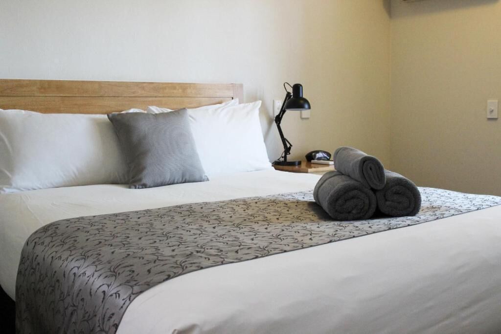 Una cama bien hecha con una colcha estampada, un cabecero de madera y una lámpara de noche.