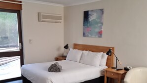 Habitación de hotel con cama, mesita de noche, lámpara, silla, ventilador de techo y un cuadro en la pared.
