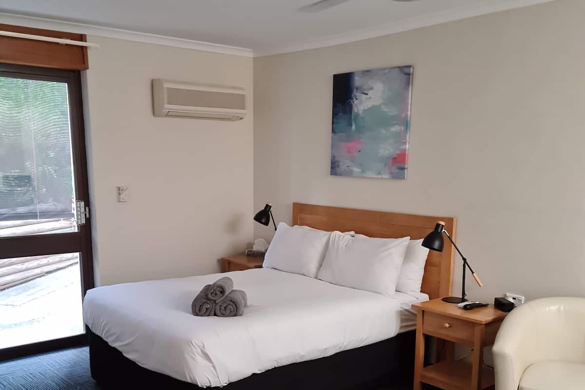 A hotel room with a bed, a nightstand, a lamp, a chair, a ceiling fan, and a painting on the wall.