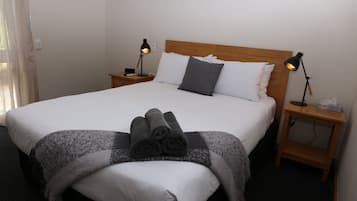 Ein ordentlich bezogenes Bett mit weißen Laken und einer grauen Decke, zwei Nachttischlampen und ein Holz-Kopfteil.