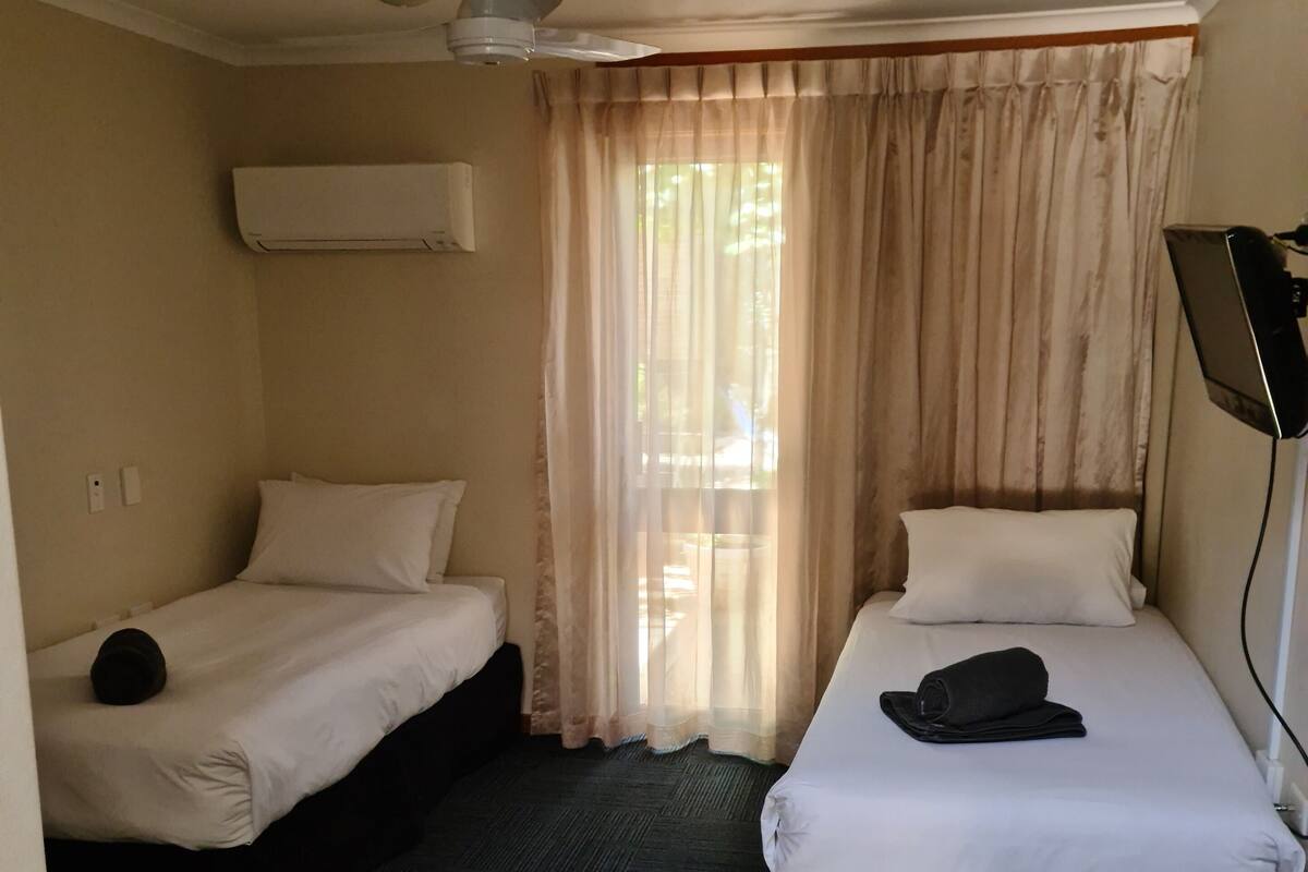 A hotel room with two beds, a desk, a chair, and a TV.