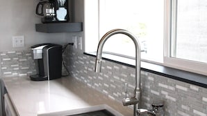 A modern kitchen with a stainless steel sink, a coffee maker, and a window with a view. - Ocean view, 100 yards to beach, pet friendly, secure fenced yard. (Bandon)