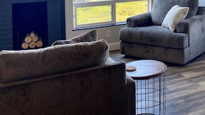 A living room with a fireplace, a gray sofa, a coffee table, and a large window offering a view of the ocean. - Ocean view, 100 yards to beach, pet friendly, secure fenced yard. (Bandon)