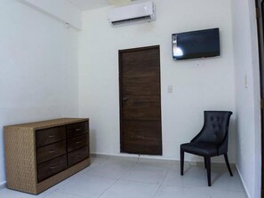Simple, functional room with a wardrobe, chair, flat-screen TV, and air conditioning.