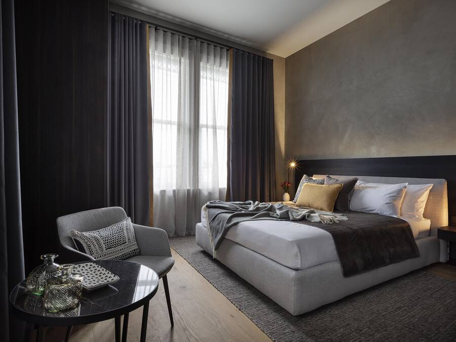 Una camera d'albergo moderna con un letto, una sedia, un tavolino e un comodino con una lampada.