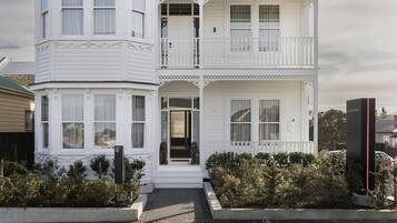 Een wit gebouw met twee verdiepingen, een balkon op de tweede etage, een voortuin en een kleine tuin.