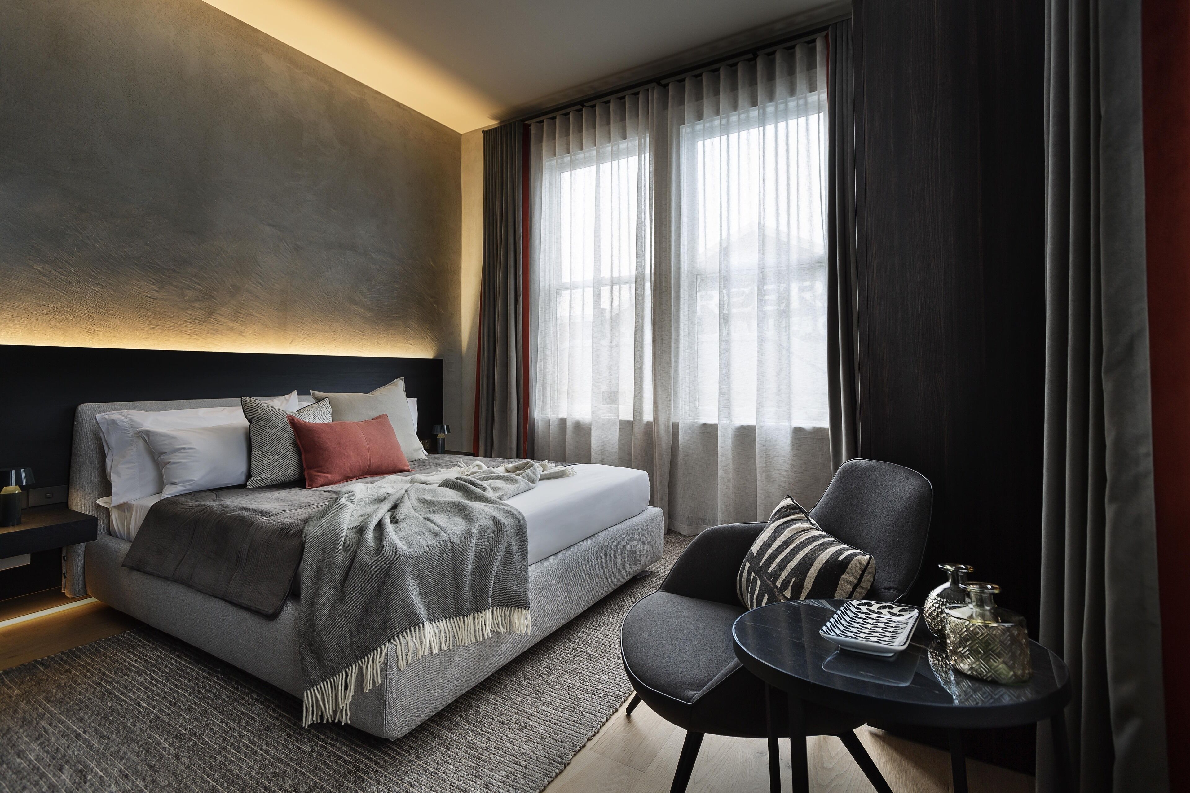 A modern bedroom with a bed, a chair, a small table, and a window with curtains.