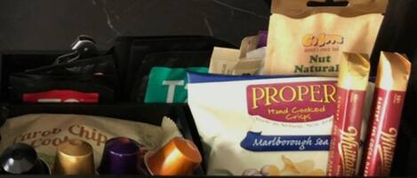 Een keukulaagje met verschillende etenswaren, waaronder een zak 'PROPER Hand Cooked Crisps', een zak 'Nut Natural' en wat 'Carob Chip Cookies'.