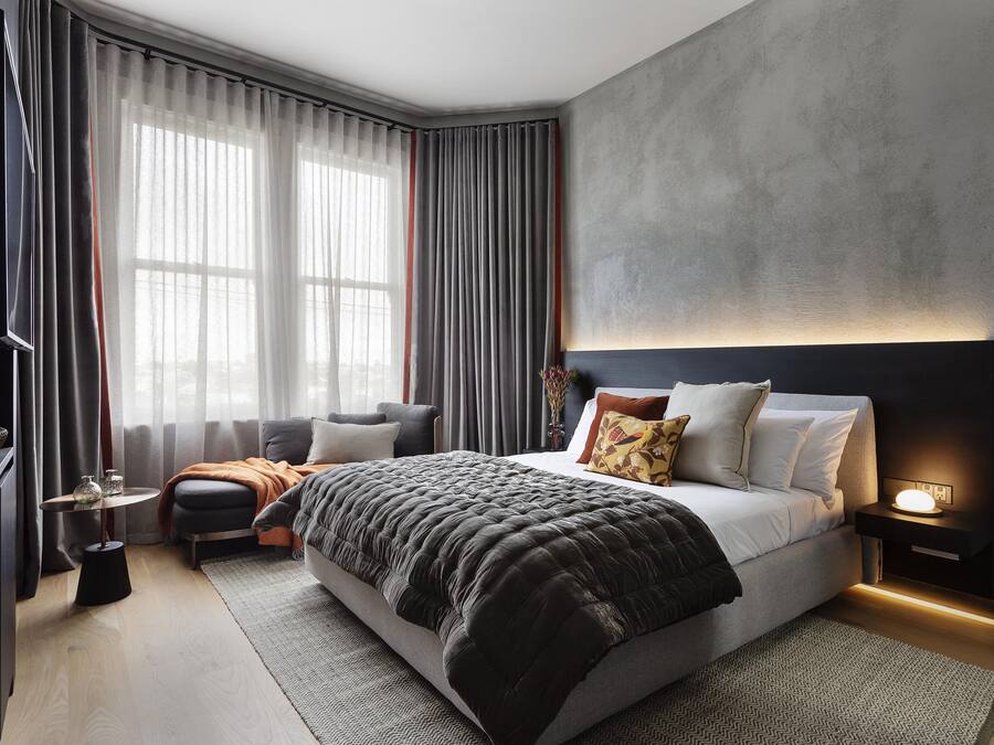 Ein modernes Schlafzimmer mit einem großen Bett, Nachttischen, einem Fernseher und Blick ins Freie durch transparente Vorhänge.
