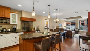 A kitchen with a central island, bar stools, wooden cabinets, a microwave, and a large window providing a view of the outdoors. -  Mountain Luxury Resort (Canmore)
