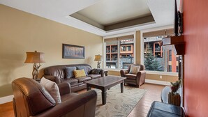 A living room with a brown leather sofa, a coffee table, and a TV on a stand. -  Mountain Luxury Resort (Canmore)