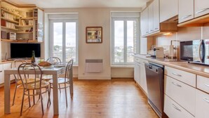 Una cocina moderna con armarios blancos, una mesa de comedor con sillas y vistas de la ciudad a través de grandes ventanales.